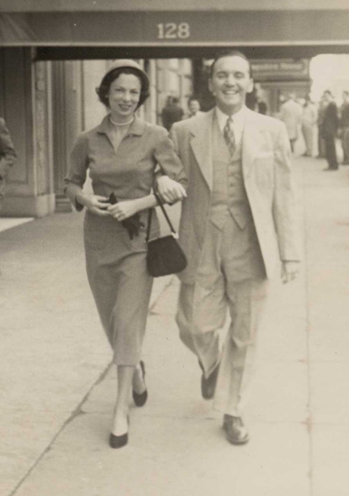 Bertha Rose and Lester Sr. walking arm in arm along a city pavement, both smiling, beneath an awning marked 128.